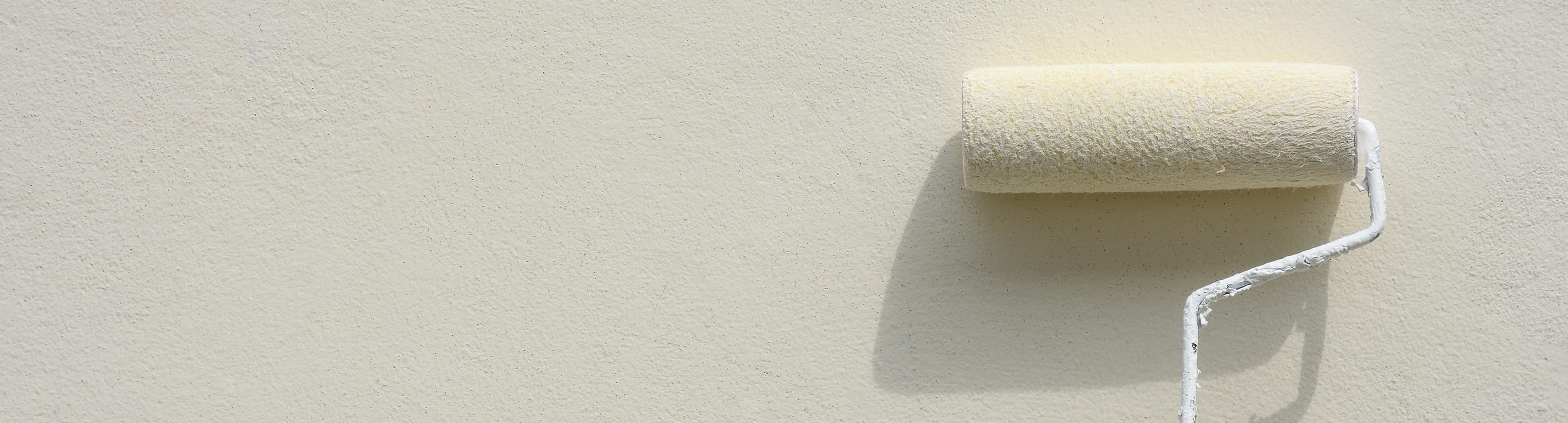 A paint roller against a freshly finished wall