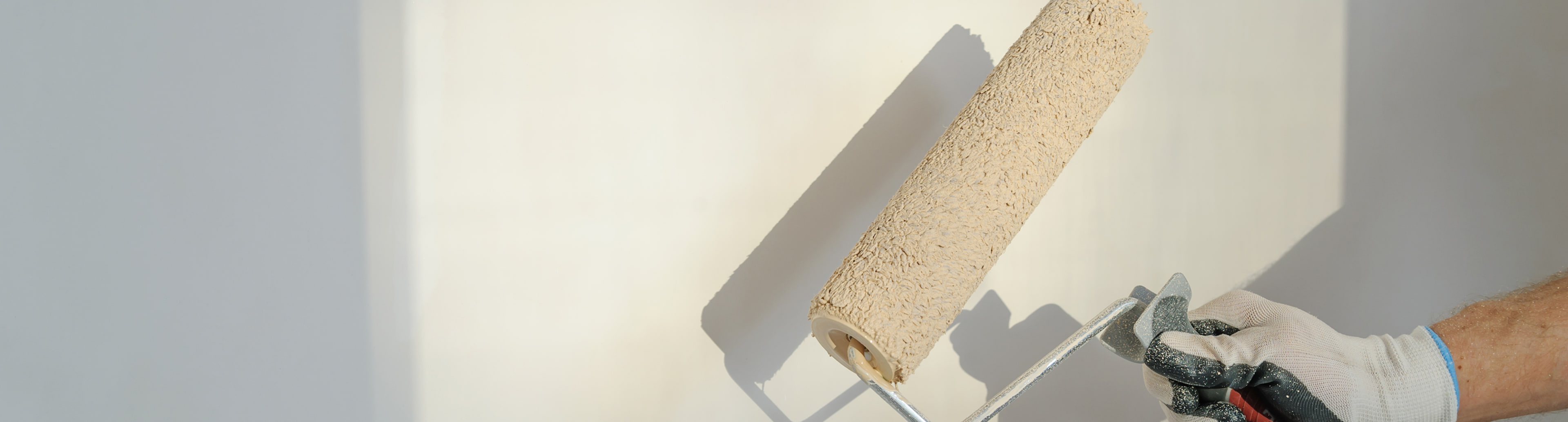 Gloved hand rolling beige paint onto a wall