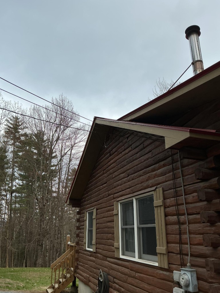 Log cabin side with brown logs and tan shutters before painting